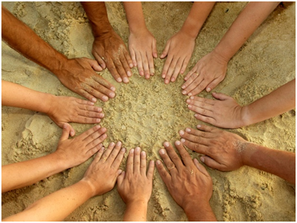 Children's hands in a circle in the sand.
